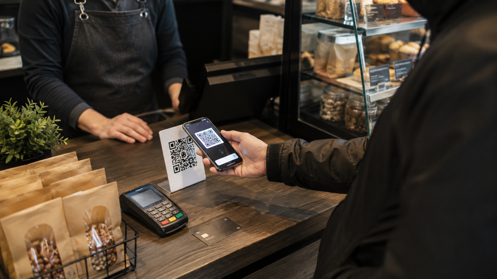 Клиент оплачивает покупку по QR-коду через смартфон в кафе, на прилавке терминал безналичной оплаты